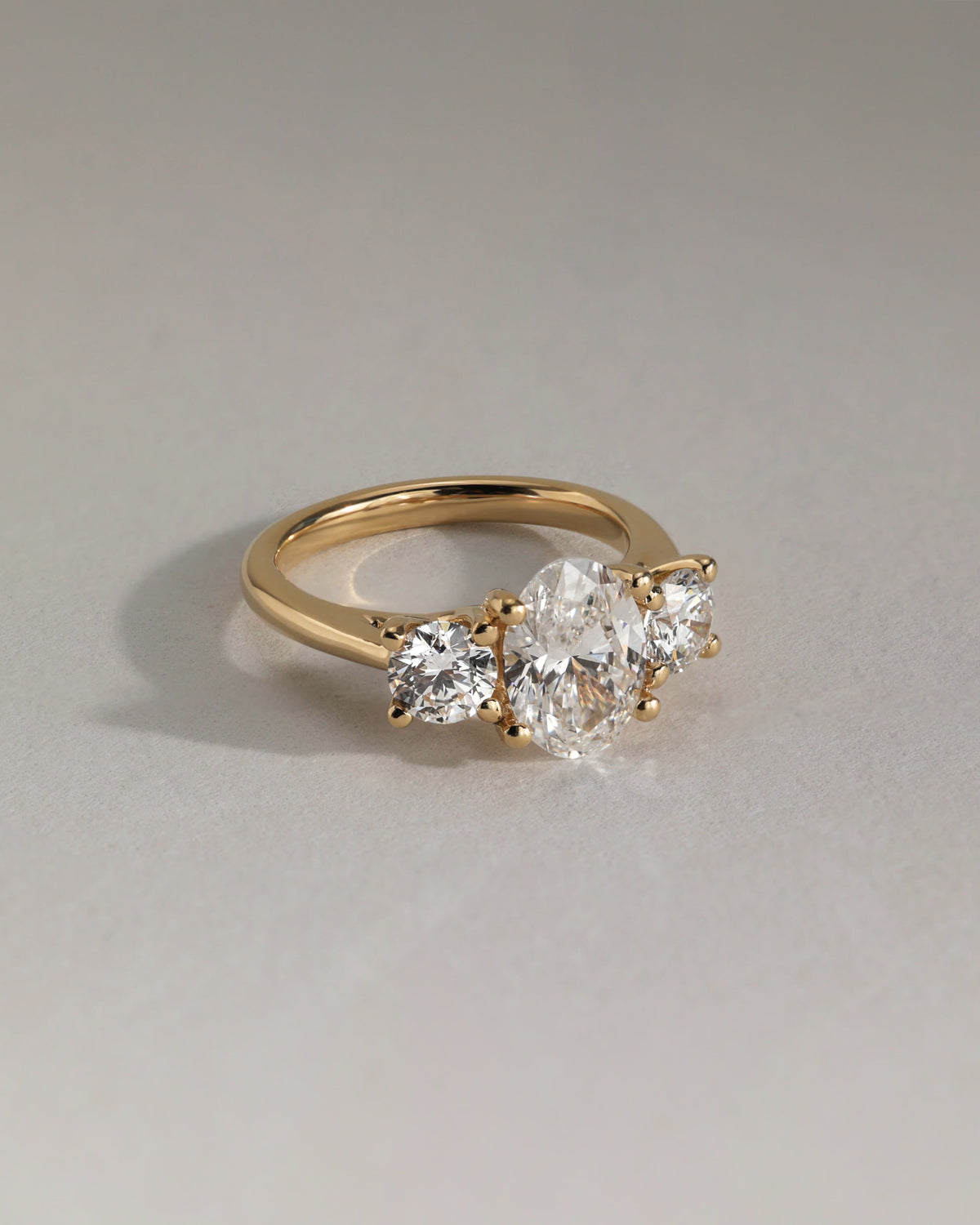 Grace - Oval Claw Trilogy with Round Side Stones, Open Trellis Gallery and Tapered Band Engagement Ring - Yellow Gold